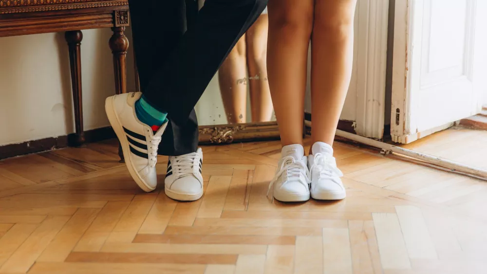 Gros plan des pieds d'un couple en baskets blanches sur un parquet