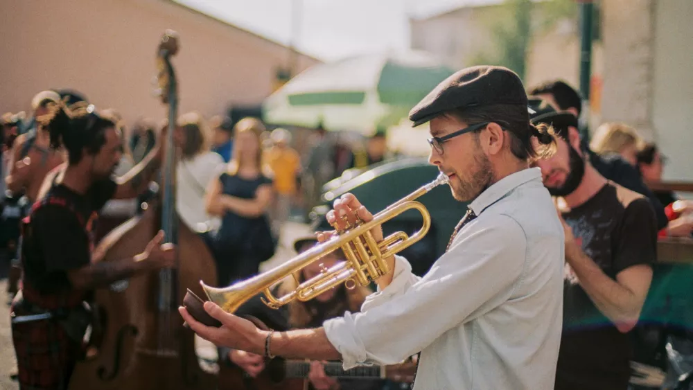 A trumpet player performing outdoors in daylight, surrounded by a standing crowd
