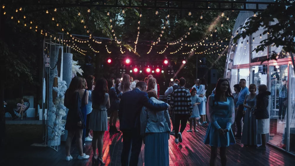 People gathered on an open-air wooden floor at night, under strings of warm lights