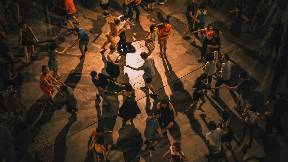 Vue de dessus d'une trentaine de couples dansant le swing sur une place pavée, de nuit, avec de longues ombres sur les dalles