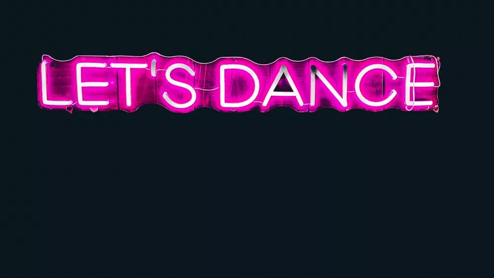Pink neon sign reading LET'S DANCE glowing against a dark wall